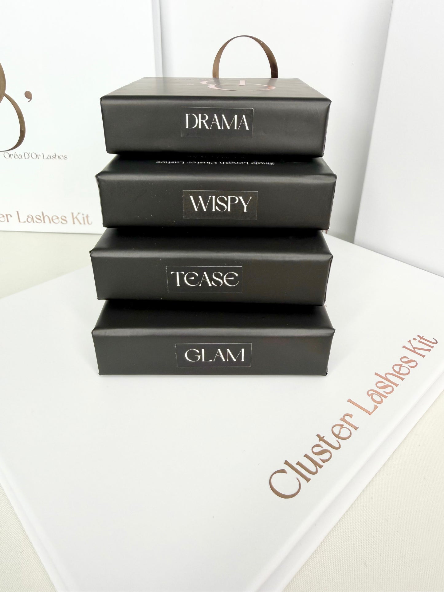 Stack of black boxes labeled 'Drama', 'Wispy', 'Tease', and 'Glam' on a white surface