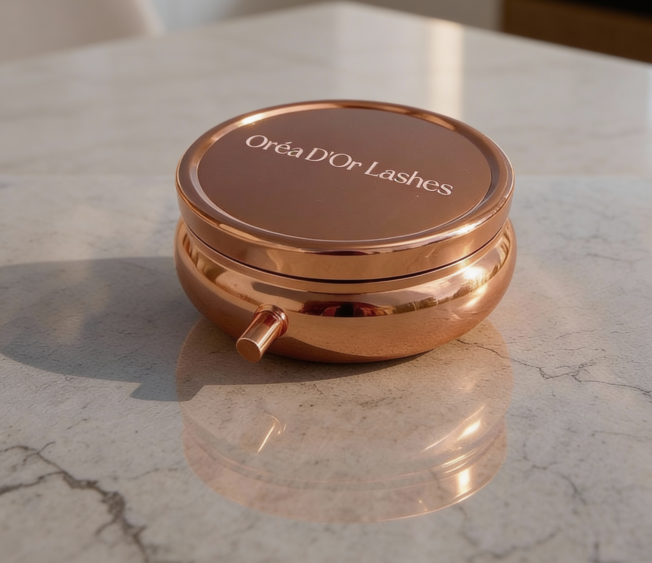 Rose gold container with 'Oréa D'Or Lashes' branding on a marble countertop.